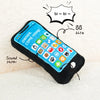 A black phone-shaped squeaky dog toy with crinkle paper is shown on a white, fluffy surface.