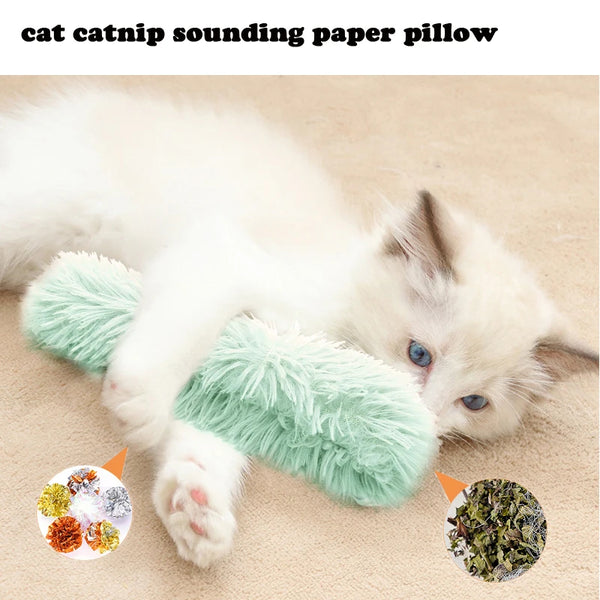 A white kitten lying on a beige surface next to a green catnip sounding paper pillow and loose catnip material.