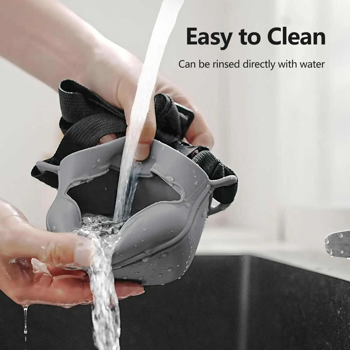 Hands are rinsing a gray silicone dog treat pouch directly with water.