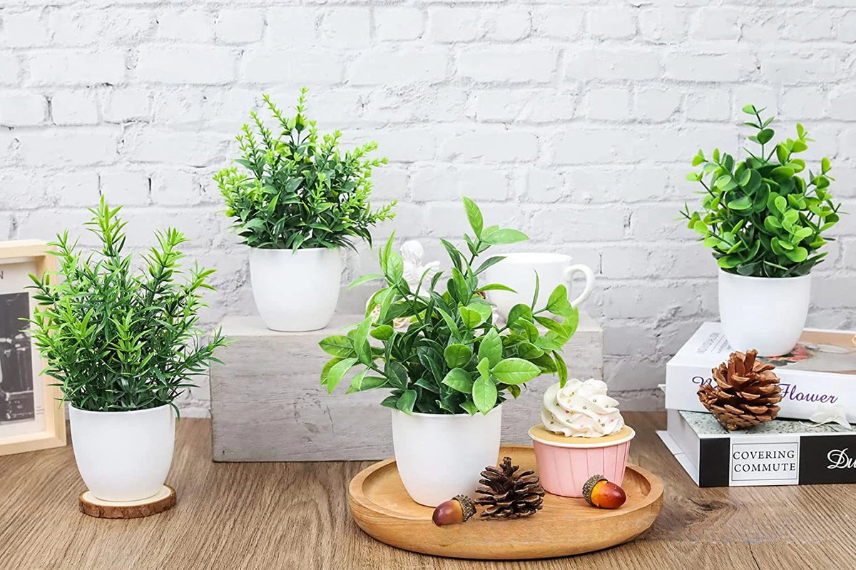 A collection of artificial bonsai potted plants in white ceramic pots displayed on a wooden surface.