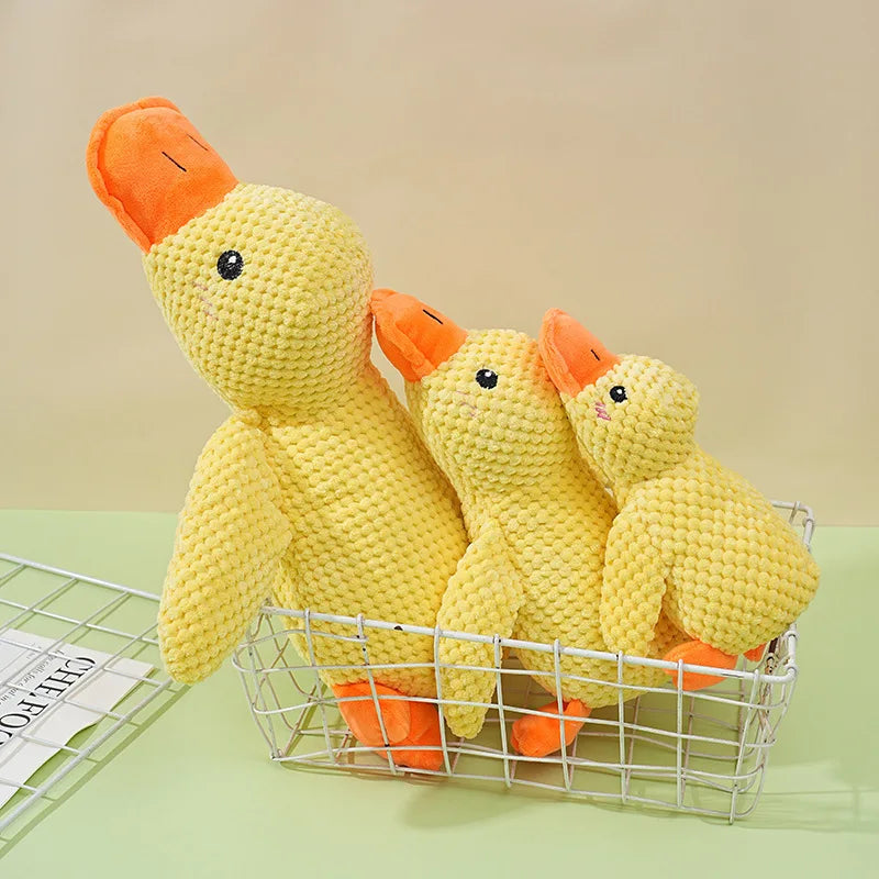 A yellow plush duck dog toy is shown in a wire basket on a light green surface.