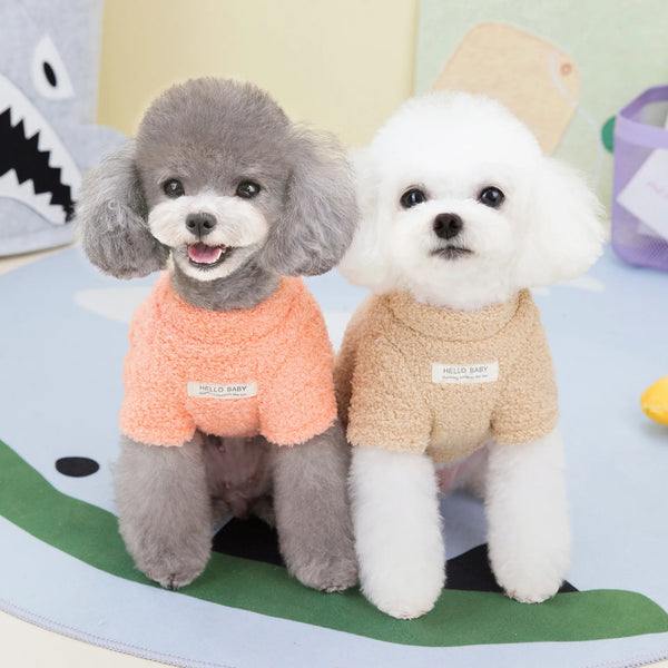 Two plush dogs wearing knitted sweaters, one gray and one white, sitting on a green surface.