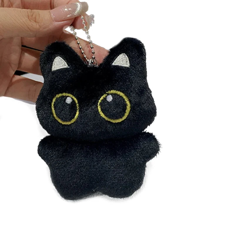 A black cat plush pendant with silver chain and sparkly ears being held by a hand.