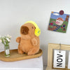 Flauschiges braunes Capybara-Plüschtier auf einem Holzbrett neben einem gerahmten Bild.