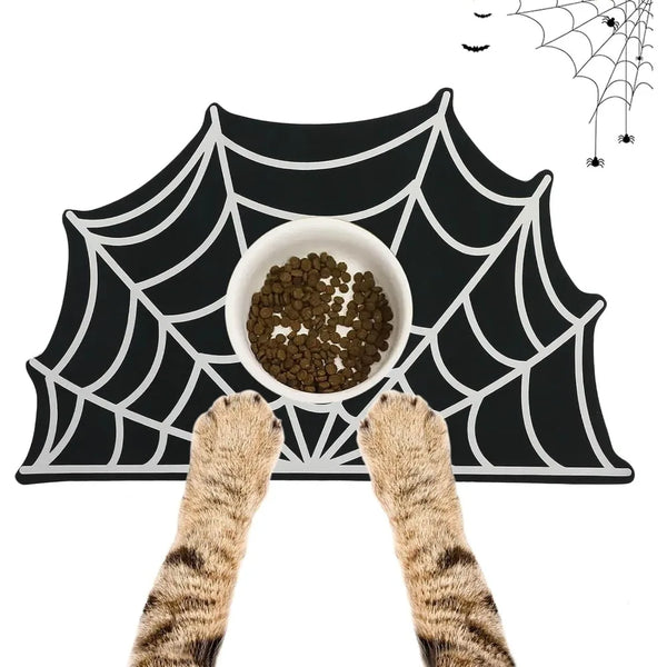 A black mat with a white spider web design features a bowl of pet food and two cat paws.
