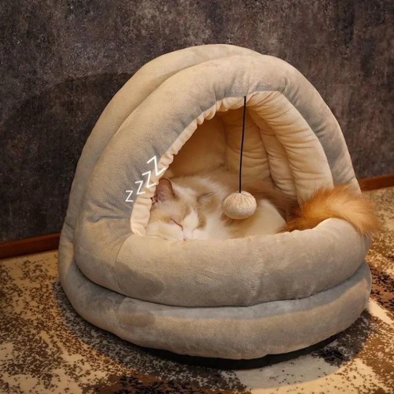 A fluffy white cat is sleeping inside a beige plush cat nest bed with a hood.