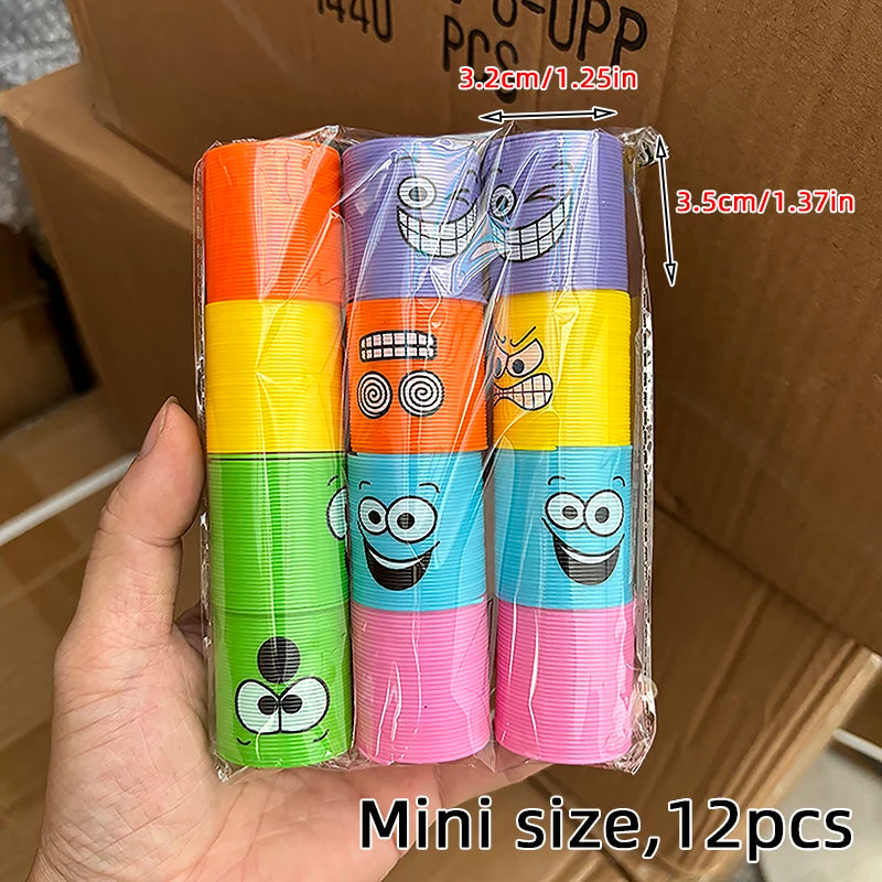 A hand holds a clear plastic package containing 12 colorful spring coil toys in rainbow colors.