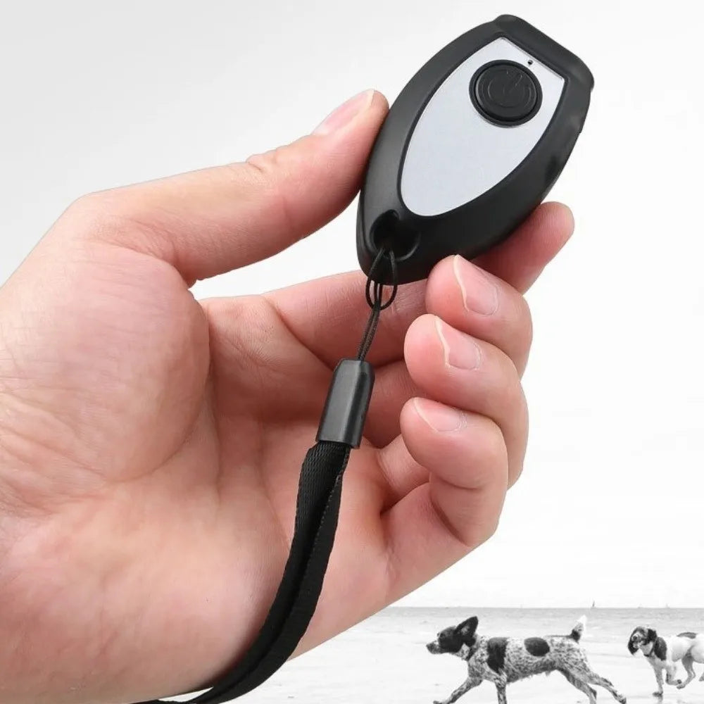 A hand holds a black handheld ultrasonic dog bark deterrent device with an LED light attached by a strap.
