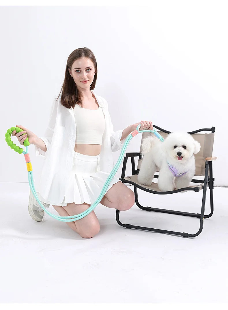 A woman is holding an adjustable hands-free dog leash with a green handle and a light blue cord, next to a white poodle.