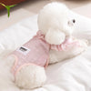 A fluffy white dog wearing pink ruffled shorts lying on a white surface.