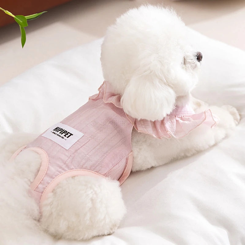 A fluffy white dog wearing pink ruffled shorts lying on a white surface.