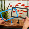 Manos sostienen un bebedero de pescado multiforma azul y negro con pequeños peces rojos flotando en el agua.