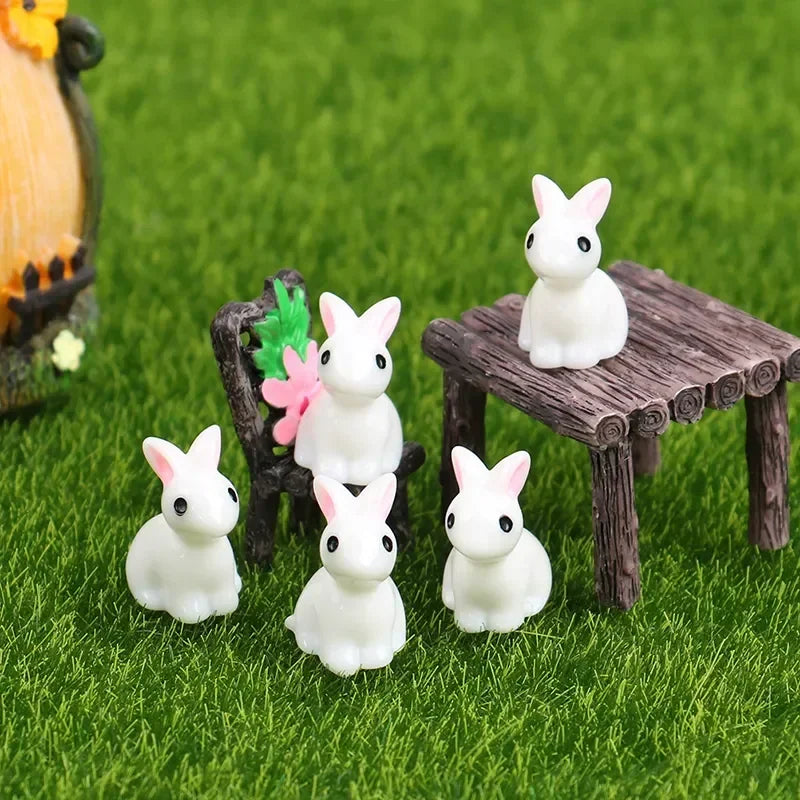 A set of white resin bunny figurines displayed on green grass next to a wooden table.