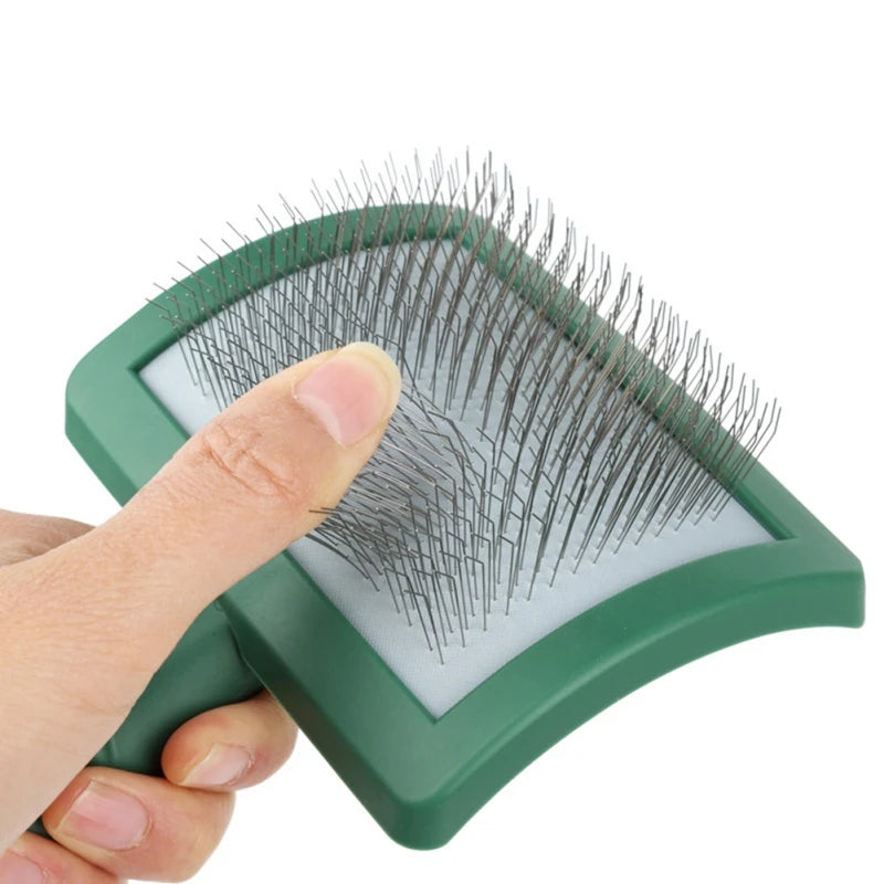 A hand holds a green slicker brush with numerous long, thin bristles for grooming.