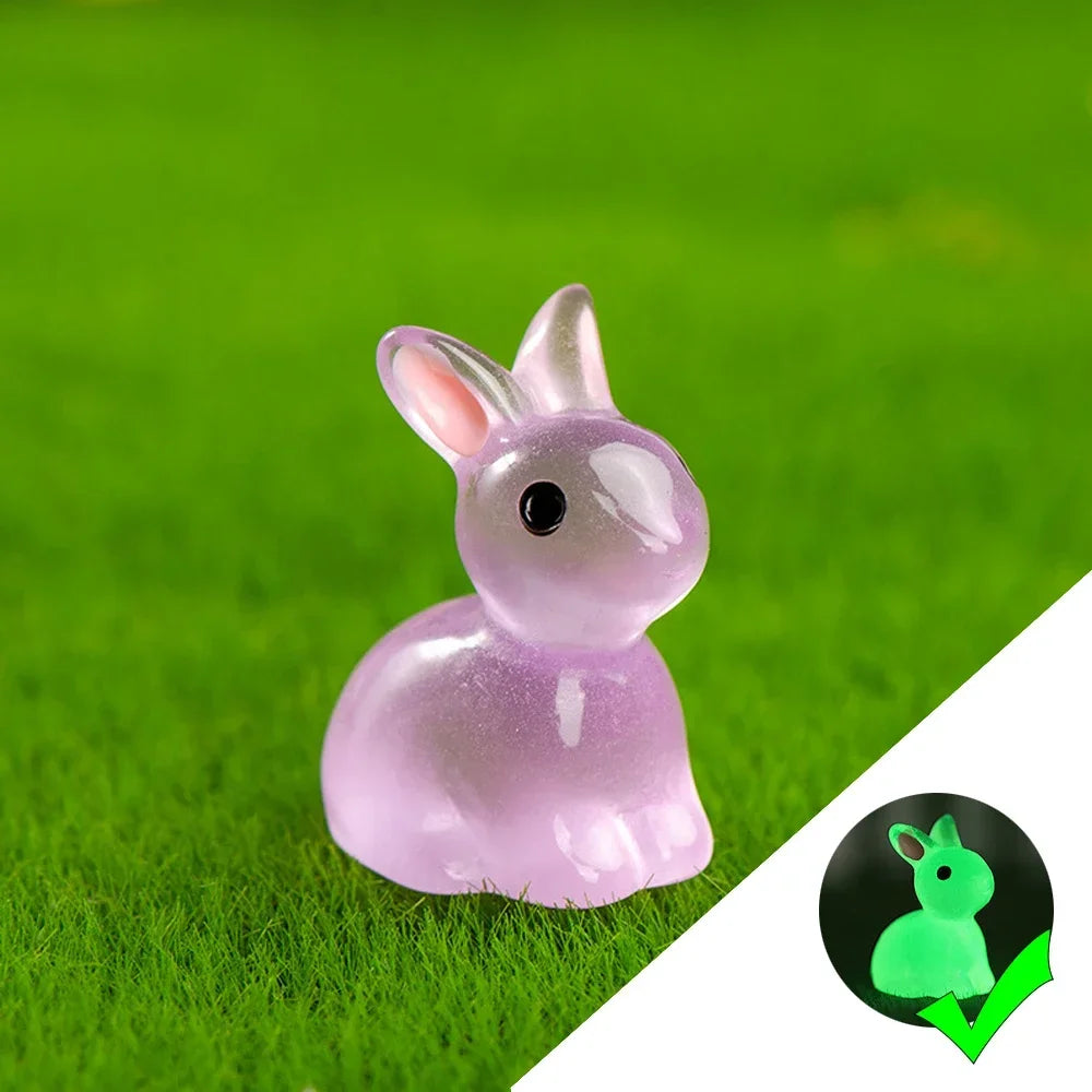 A small, translucent pink glow-in-the-dark resin bunny figurine sitting on bright green grass.