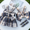 A plaid fabric bow and harness dress displayed on a white surface next to a magazine.