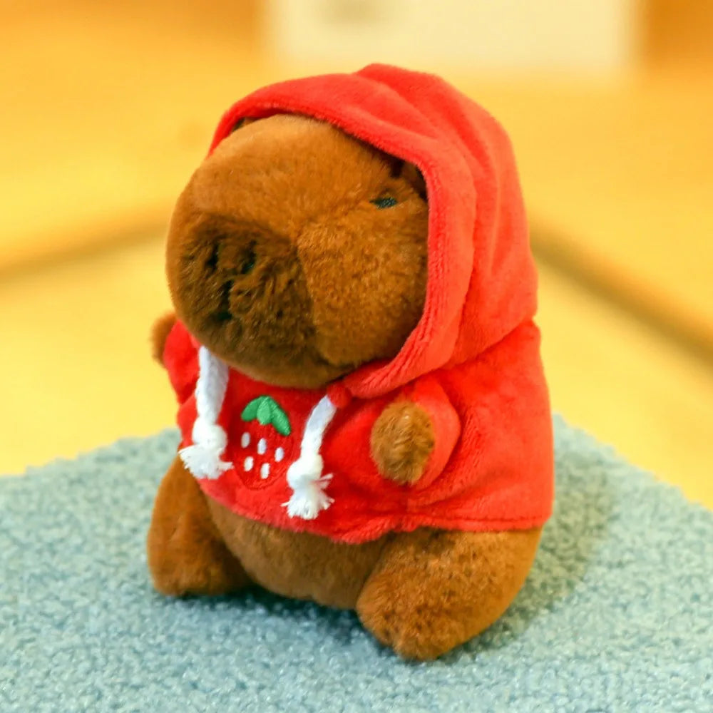 Orangefarbene Capybara-Plüschpuppe mit rotem Hoodie, weißer Borte und grünen Akzenten.