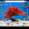 A vibrant red artificial pine tree plant is displayed in a clear aquarium setup with small fish and white gravel.