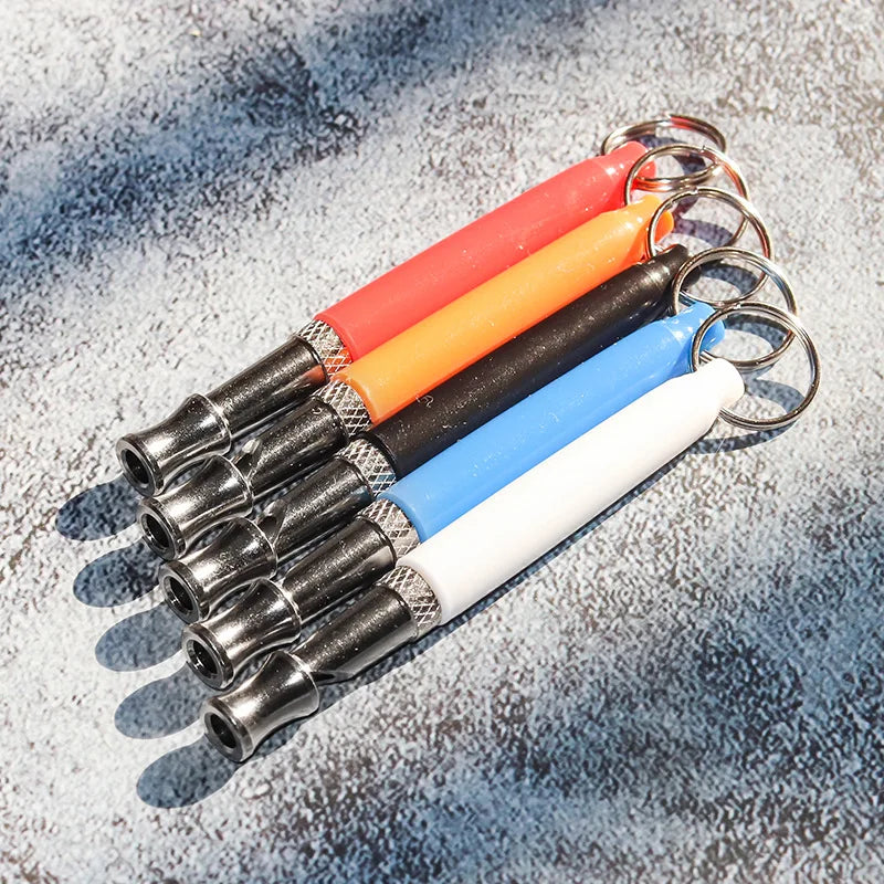 A set of colorful ultrasonic dog training whistles with metal clasps arranged diagonally on a gray surface.