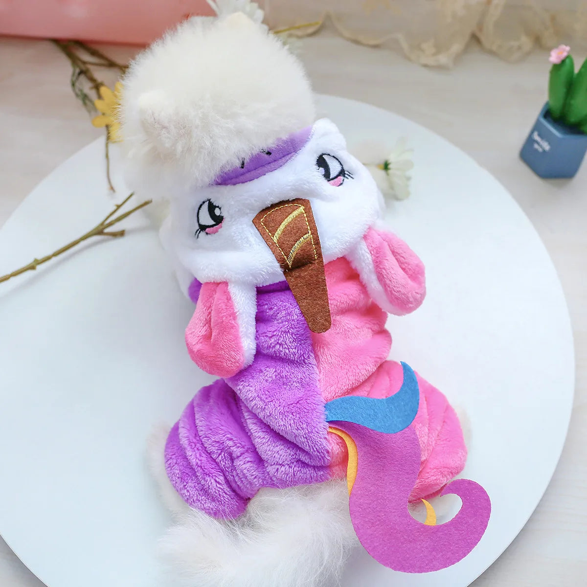 A fluffy pink and purple plush fleece outfit for a pet, resembling overalls with a white fur hood.
