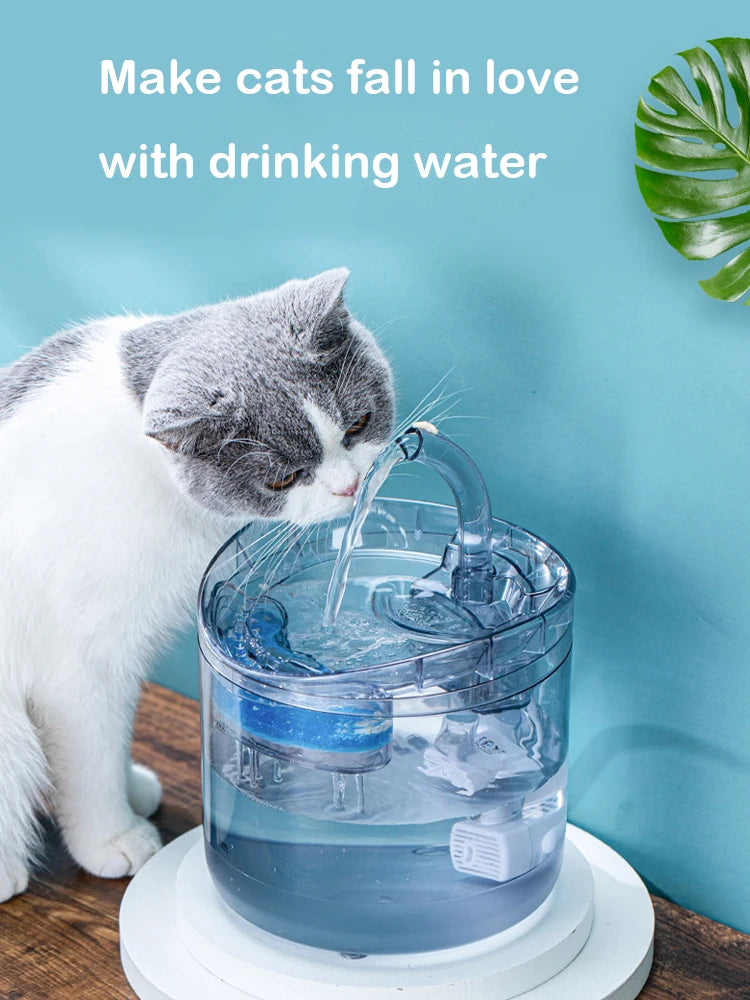 A gray and white cat is drinking water from a motion-activated pet water fountain.