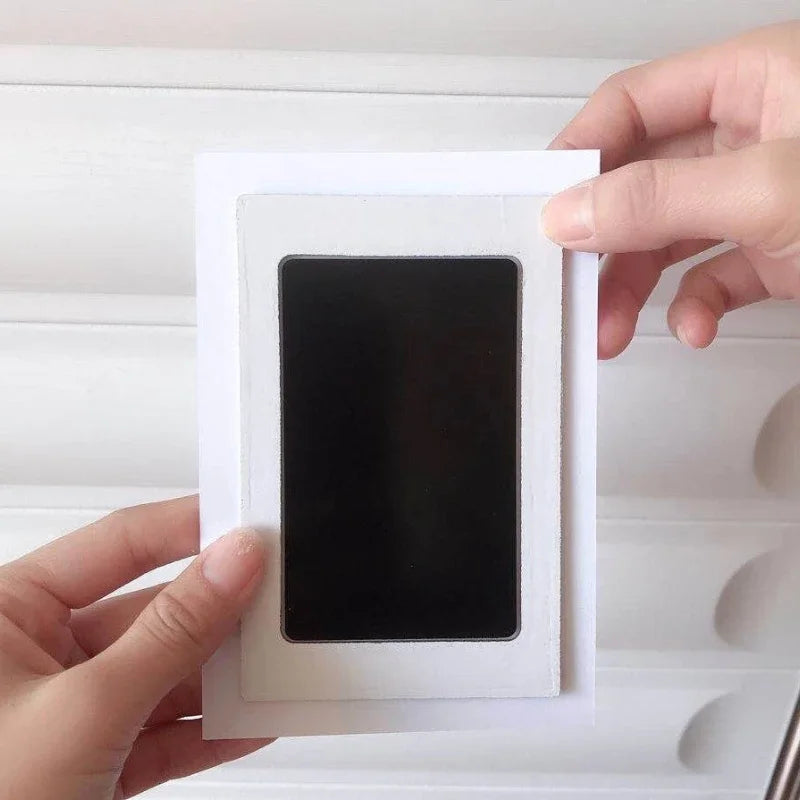 Un kit d'empreinte de main avec une impression carrée noire est tenu sur un fond blanc.