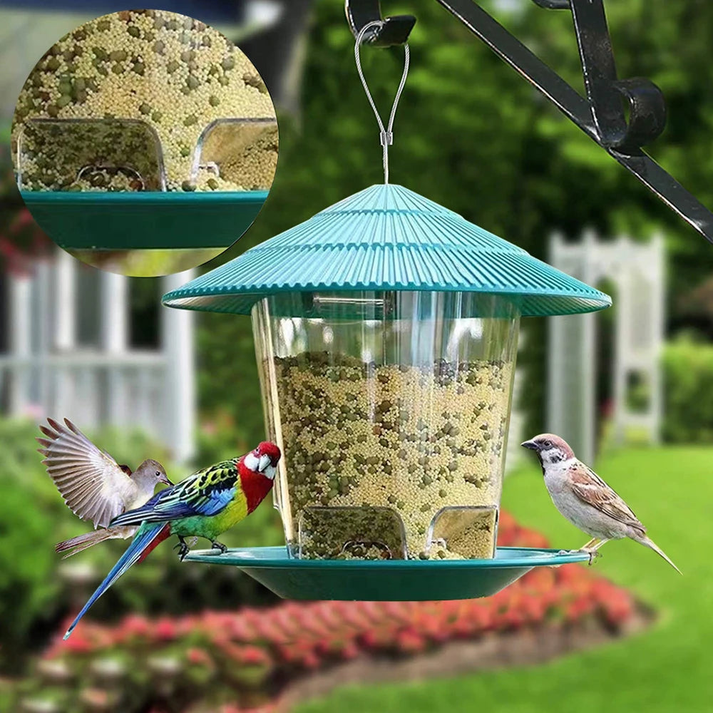 A hanging bird feeder with a teal dome and clear glass bowl filled with seeds, suspended by a metal hook.
