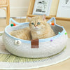 A fluffy orange tabby cat is relaxing in a woven cat scratcher and comfort bed filled with colorful play balls.