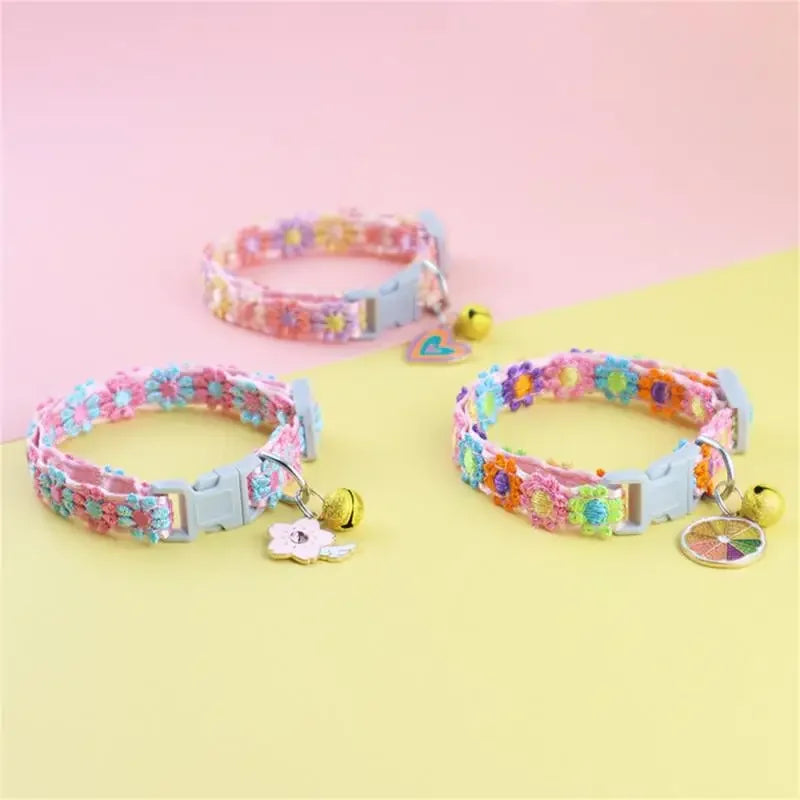 A pink and purple rainbow flower cat collar with a gold bell displayed on a yellow background.