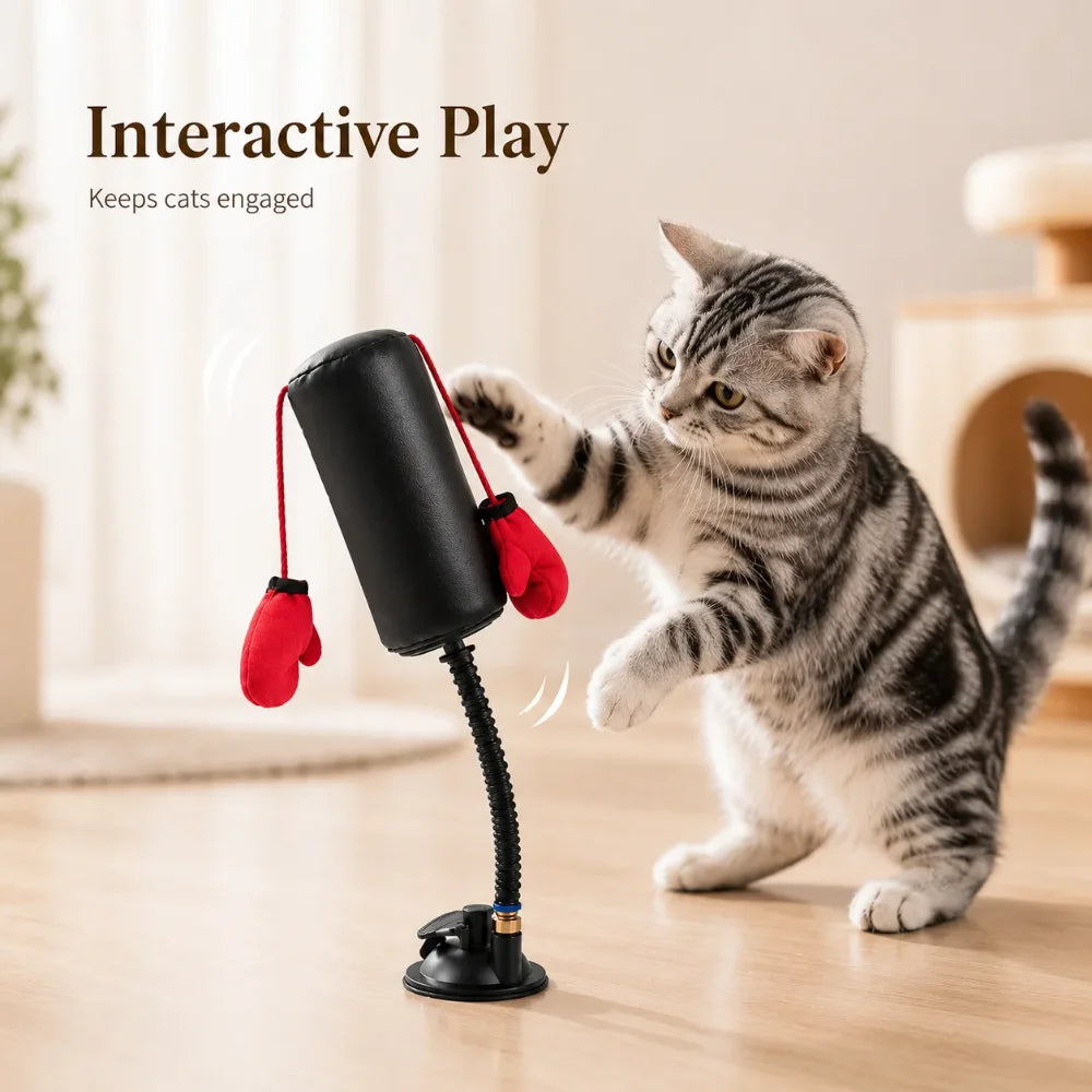 A tabby cat is playing with an interactive cat boxing bag and red boxing gloves on a wooden floor.