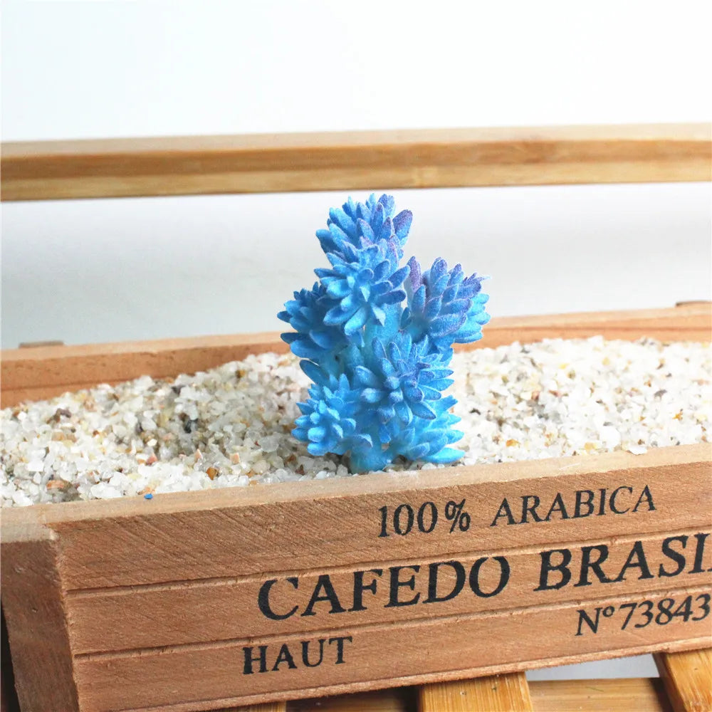 Blue artificial succulent plant in a wooden box with light gravel.