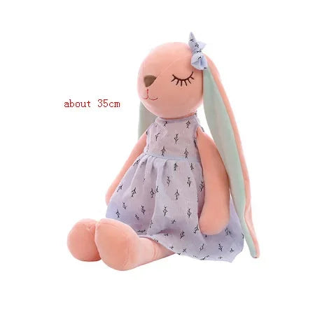 A light pink kawaii plush rabbit stuffed animal toy with a purple patterned dress and a bow.
