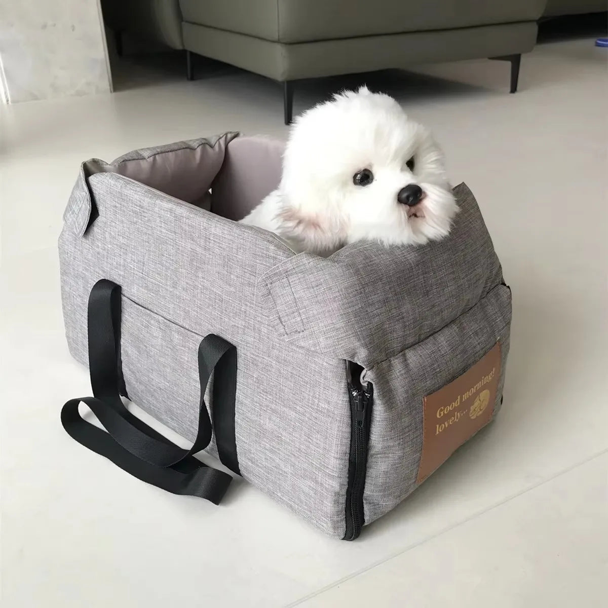 A gray portable pet car seat carrier is shown with a fluffy white dog resting inside.