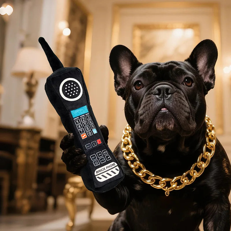 A black pug holds a plush phone-shaped squeaky dog toy with crinkle paper in a luxurious interior setting.
