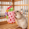 A small brown rodent is interacting with a pink, textured chewing toy shaped like a cake and topped with a green blob inside 