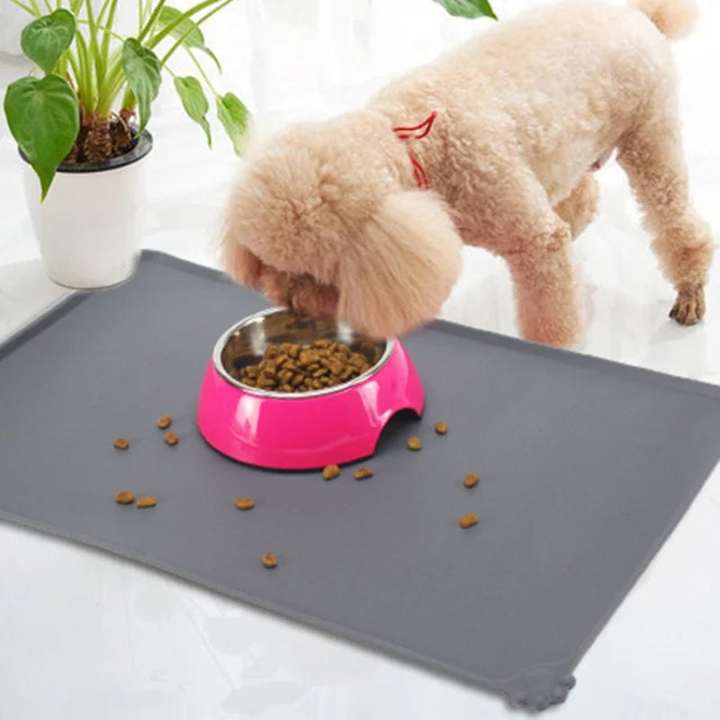 A fluffy light brown dog is feeding from a pink silicone bowl on a gray waterproof pet feeding mat.
