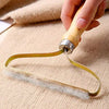 A hand is using a double-sided fabric and pet hair remover brush on a light beige fabric surface.