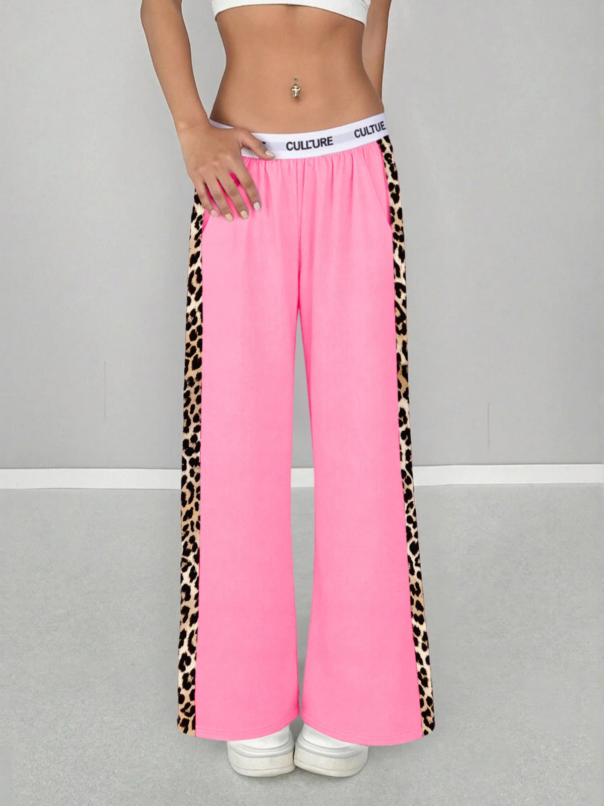 A woman wearing bright pink leopard print high-waist wide leg pants and a white crop top.