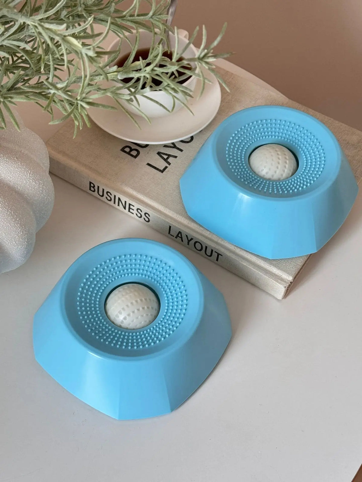 Un cuenco para perros interactivo de color azul claro, colocado sobre un libro de madera junto a una planta en maceta.