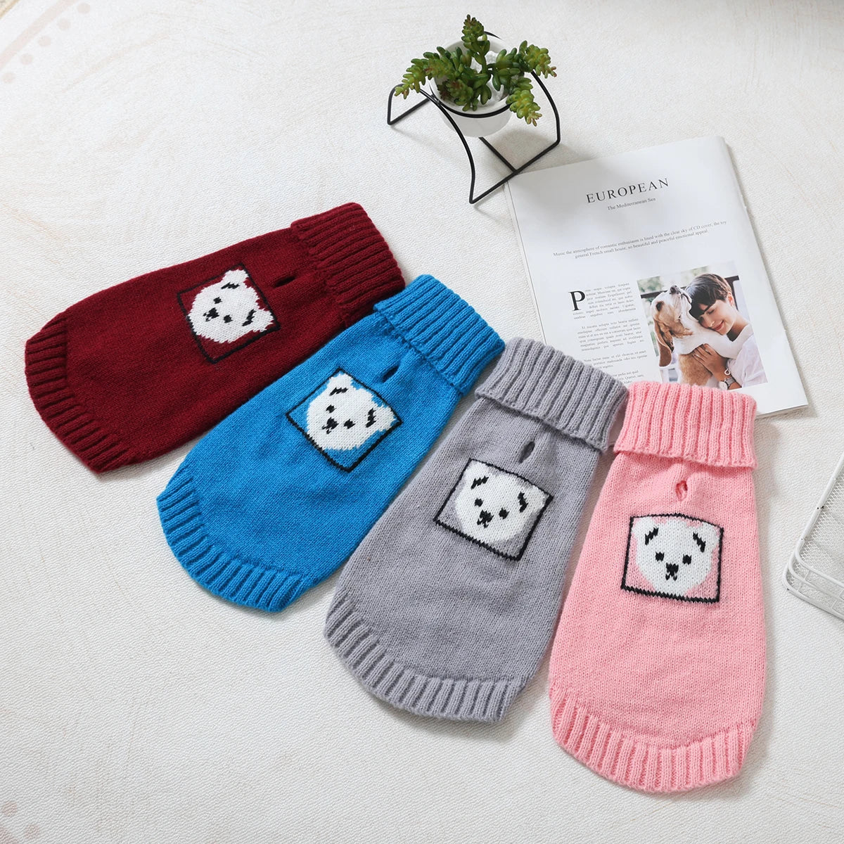 A collection of knitted winter pet sweaters in red, blue, gray, and pink, displayed on a white surface.