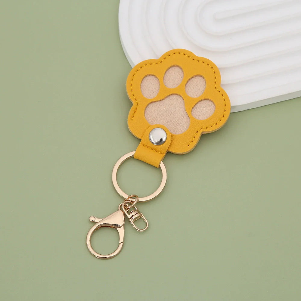 A yellow leather pet paw print airtag keepsake attached to a white textured surface.
