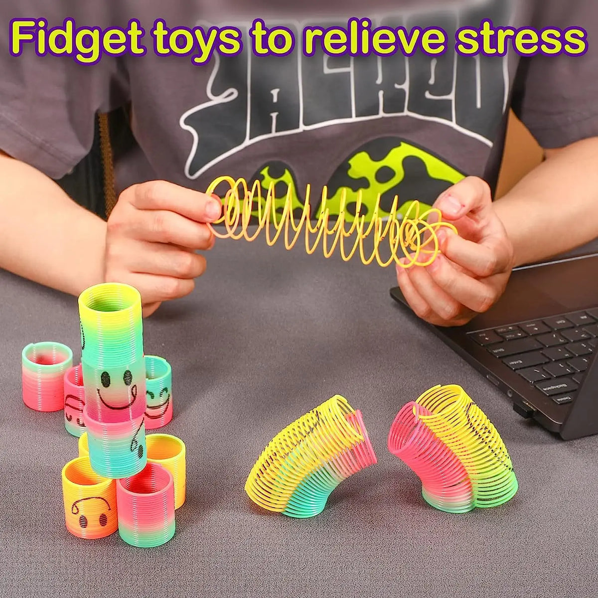 Hands are holding a yellow spring coil toy while colorful silicone fidget toys are displayed on a dark surface.