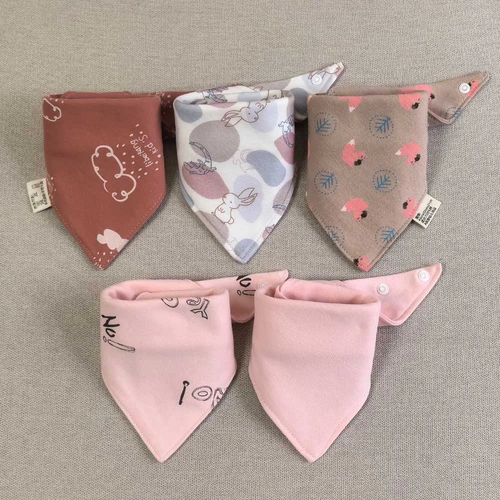 A set of five pink and beige cotton triangle baby bibs with various cartoon prints