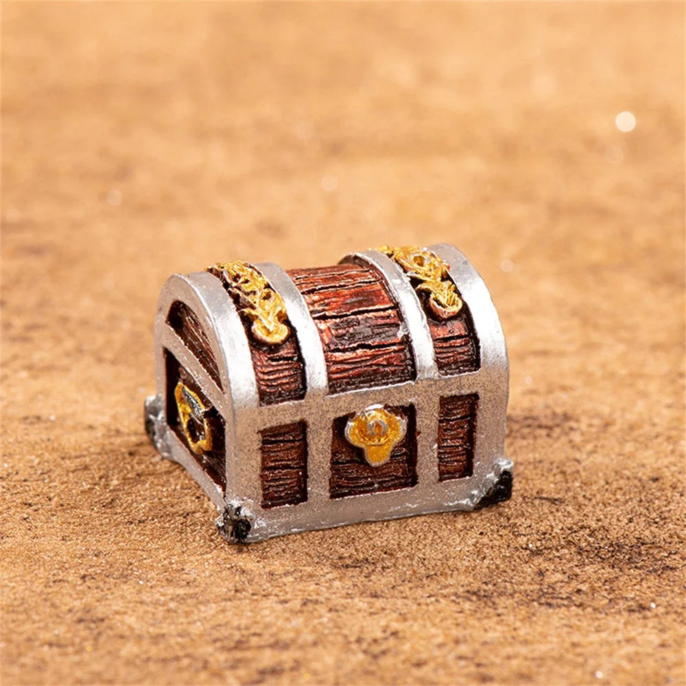 A miniature resin treasure chest ornament with a silver frame and wooden slats decorated with gold accents.