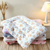 A stack of fluffy, double-sided pet blankets in various pastel colors is displayed on a wooden surface.