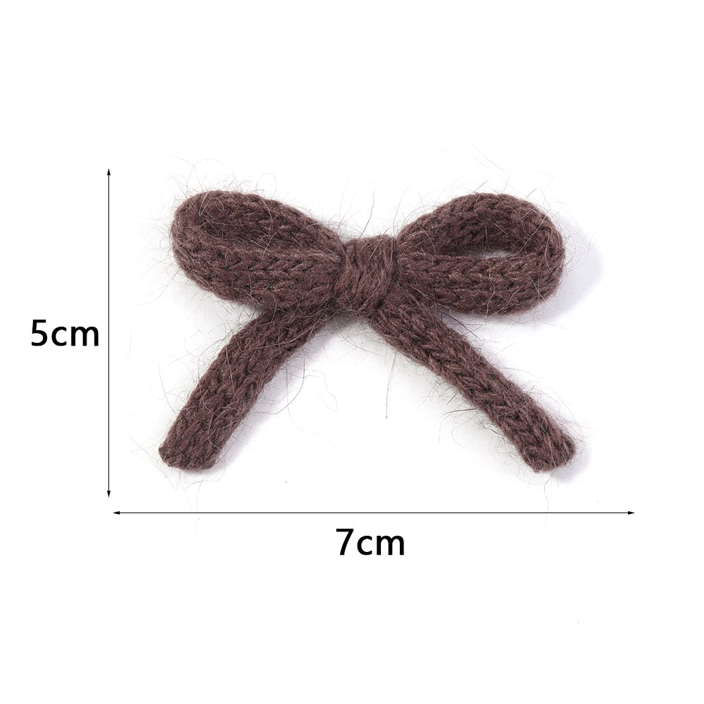 A handmade knitted cotton bow made of brown yarn, shown flat with dimensions 5cm by 7cm.