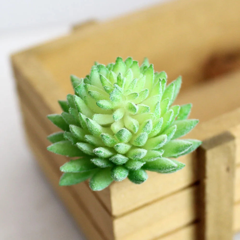A vibrant green fake succulent plant with rosette leaves is displayed in a light wooden box.