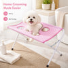 Un caniche blanc repose sur un hamac de toilettage rose pliable pour le bain et la coupe des griffes.