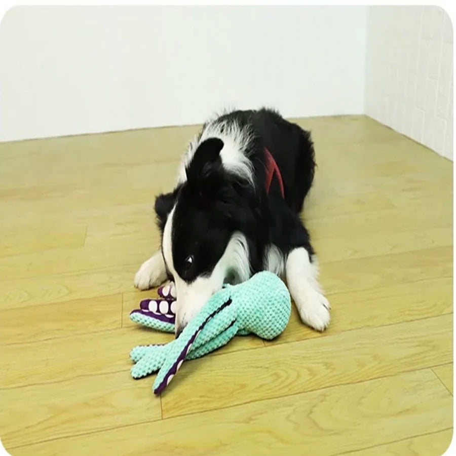 A black and white dog toy shaped like an octopus is lying on a wooden floor.