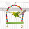 A parrot toy featuring a colorful ball necklace and wings, suspended from a green wooden bar.